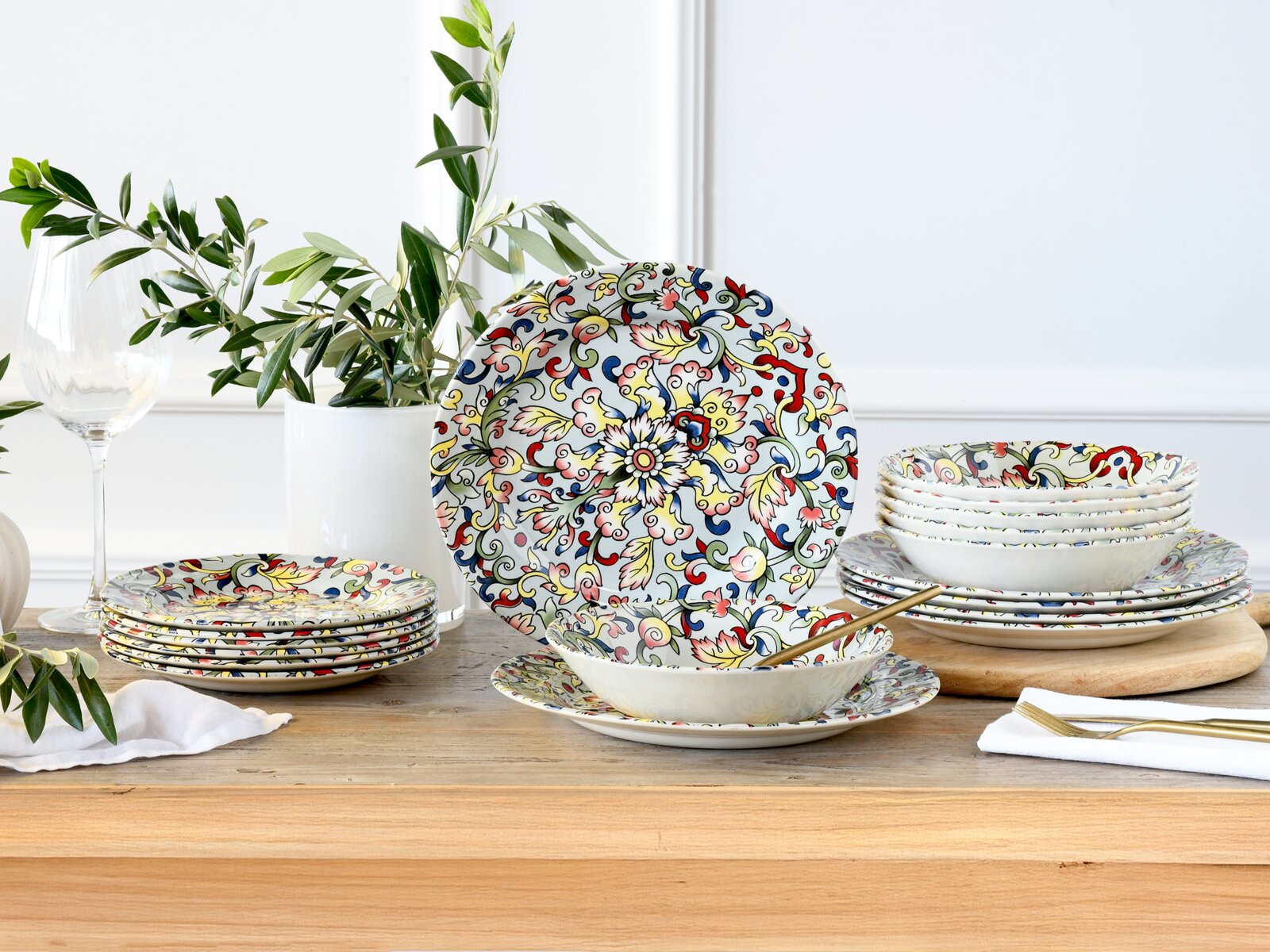 Bunt gemustertes Geschirrset aus Keramik/Porzellan mit floralen Ornamenten (Teller und Schalen) auf Holztisch dekorativ arrangiert, Perspektive: frontale Tischansicht auf Augenhöhe mit leichtem Blick von vorn.