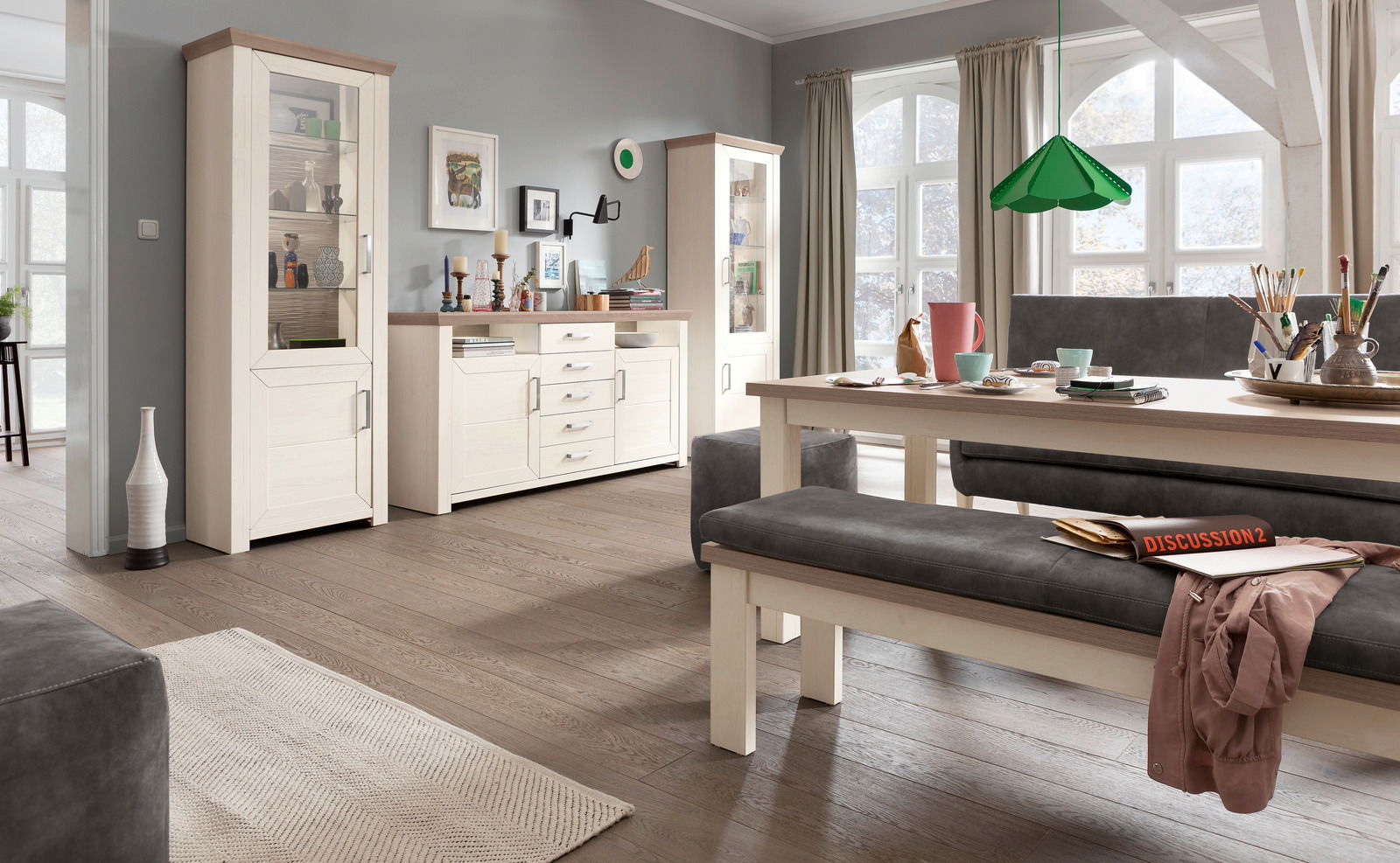 Wohnzimmer mit zwei weißen Vitrinen und einer Kommode in Holzoptik, seitliche Perspektive