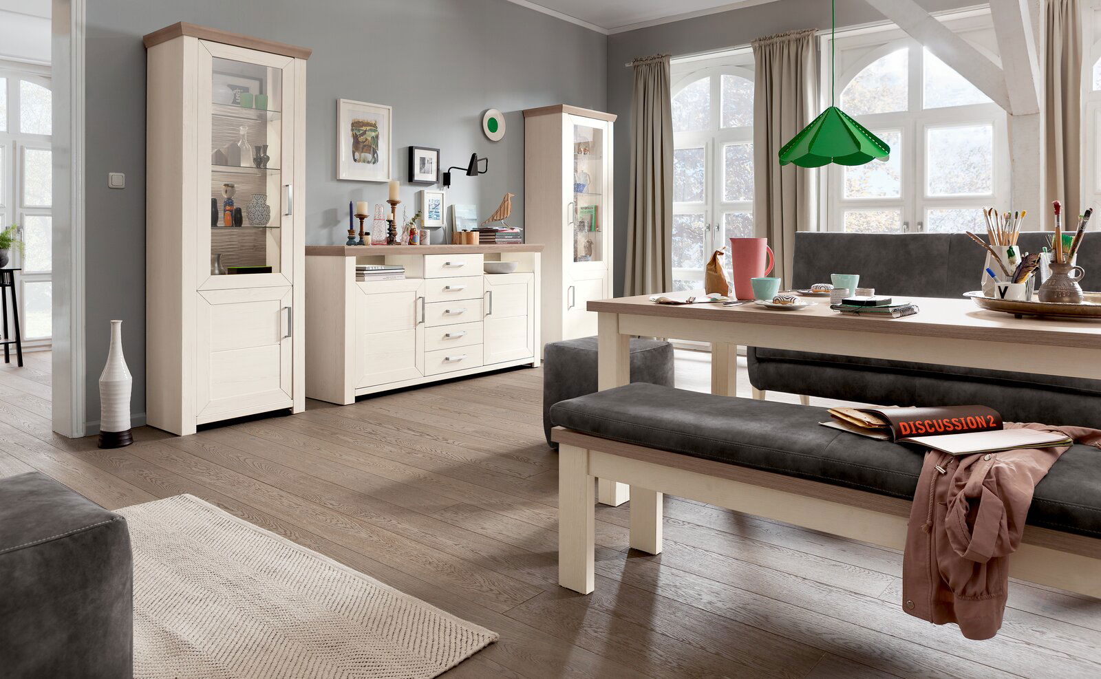 Wohnzimmer mit zwei weißen Vitrinen und einer Kommode in Holzoptik, seitliche Perspektive