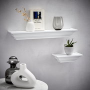 Zwei weiße Wandboards der Marke XORA, Modell VIOLA, an einer grauen Wand. Das größere Board trägt eine Vase, ein Buch und ein Glas, das kleinere eine Pflanze. Perspektive von vorne.