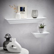 Zwei weiße Wandboards der Marke XORA, Modell VIOLA, an einer grauen Wand. Das größere Board trägt eine Vase, ein Buch und ein Glas, das kleinere eine Pflanze. Perspektive von vorne.