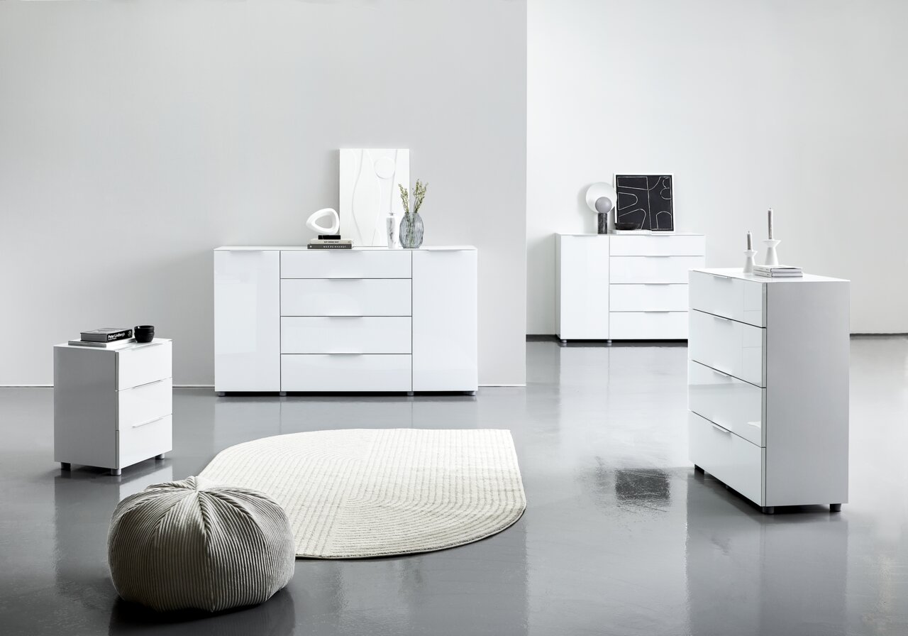 Moderne weiße Hochglanz-Kommoden in einem minimalistischen Raum, fotografiert aus einer seitlichen Perspektive.