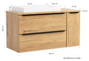 Frontansicht in leichter Schrägperspektive: moderner Waschtischunterschrank aus hellem Holz mit zwei Schubladen und schwarzer Griffleiste, rechts zusätzlicher Schrankteil, oben weißes Aufsatzwaschbecken; Maße ca. 105 x 65,5 cm.
