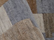Nahaufnahme eines Wollteppichs mit einem Patchwork-Design in verschiedenen Grautönen und Brauntönen, aus einer schrägen Perspektive aufgenommen.