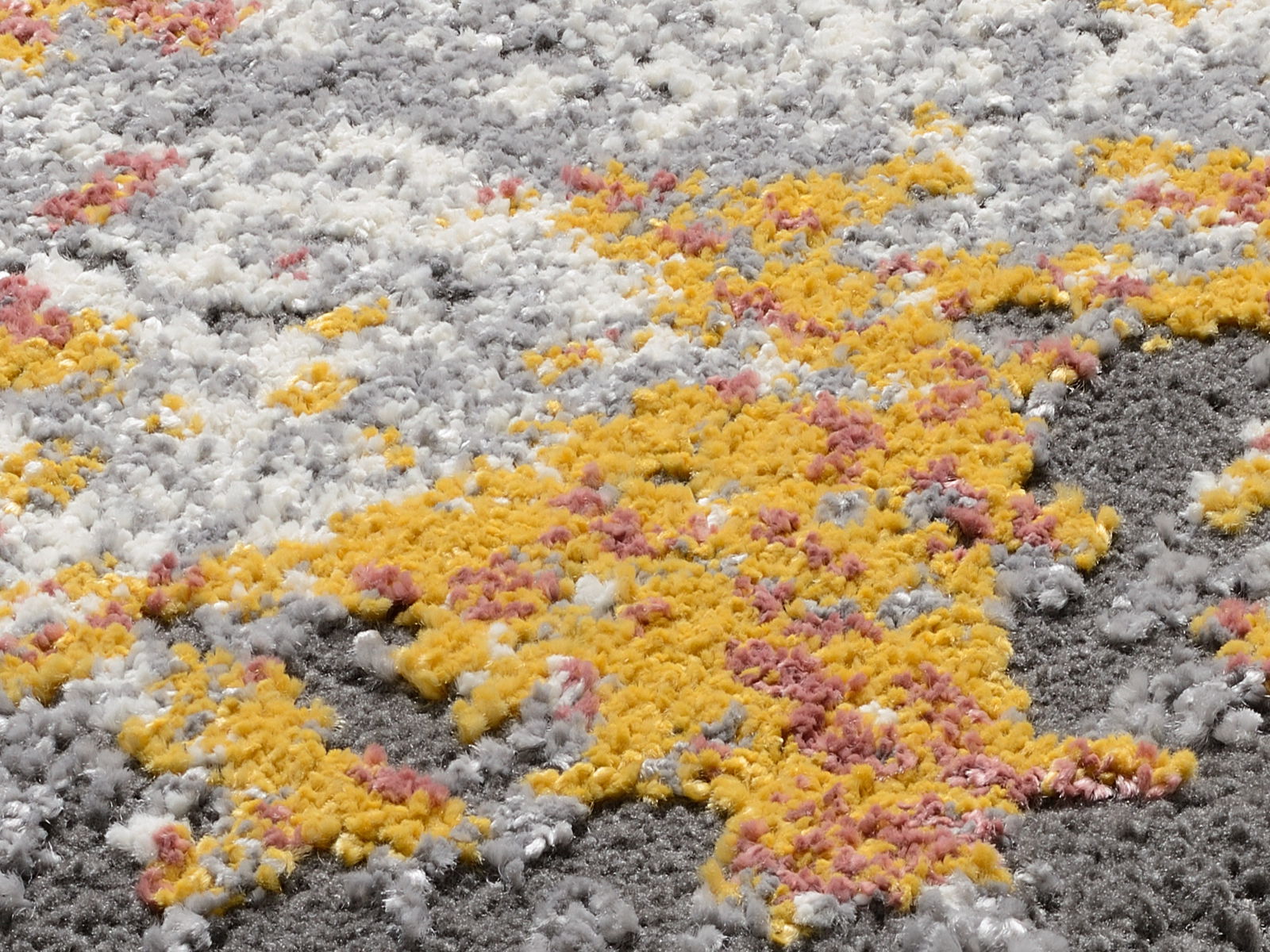 Nahaufnahme eines Designer-Teppichs mit flauschiger Textur in Gelb, Grau, Weiß und Rosa. Die Perspektive zeigt die Struktur und Farben des Teppichs aus der Nähe.