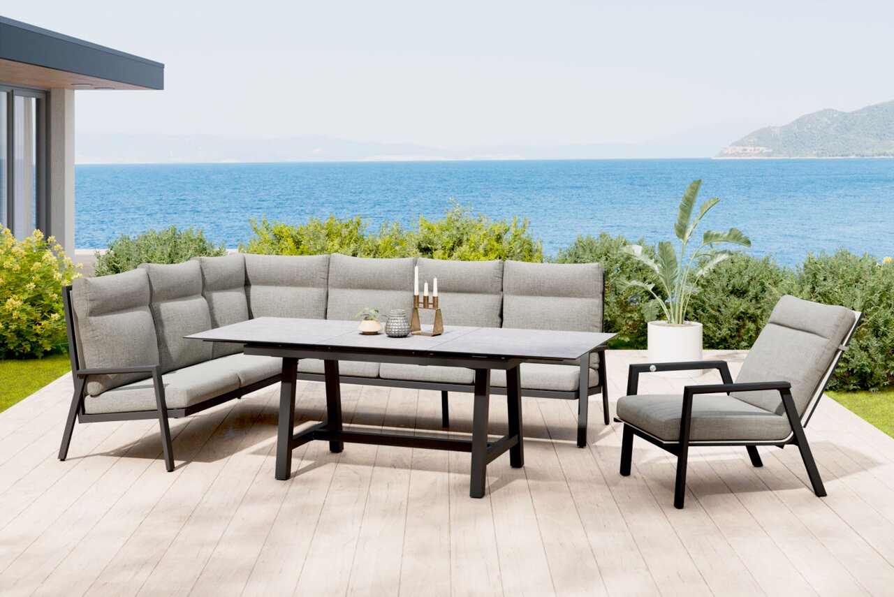 Moderne Garten-Lounge-Eckgruppe mit grauen Polstern und schwarzem Metallgestell, rechteckigem Tisch und passendem Sessel auf einer Holzterrasse mit Meerblick, frontal in leichter Schrägansicht aufgenommen