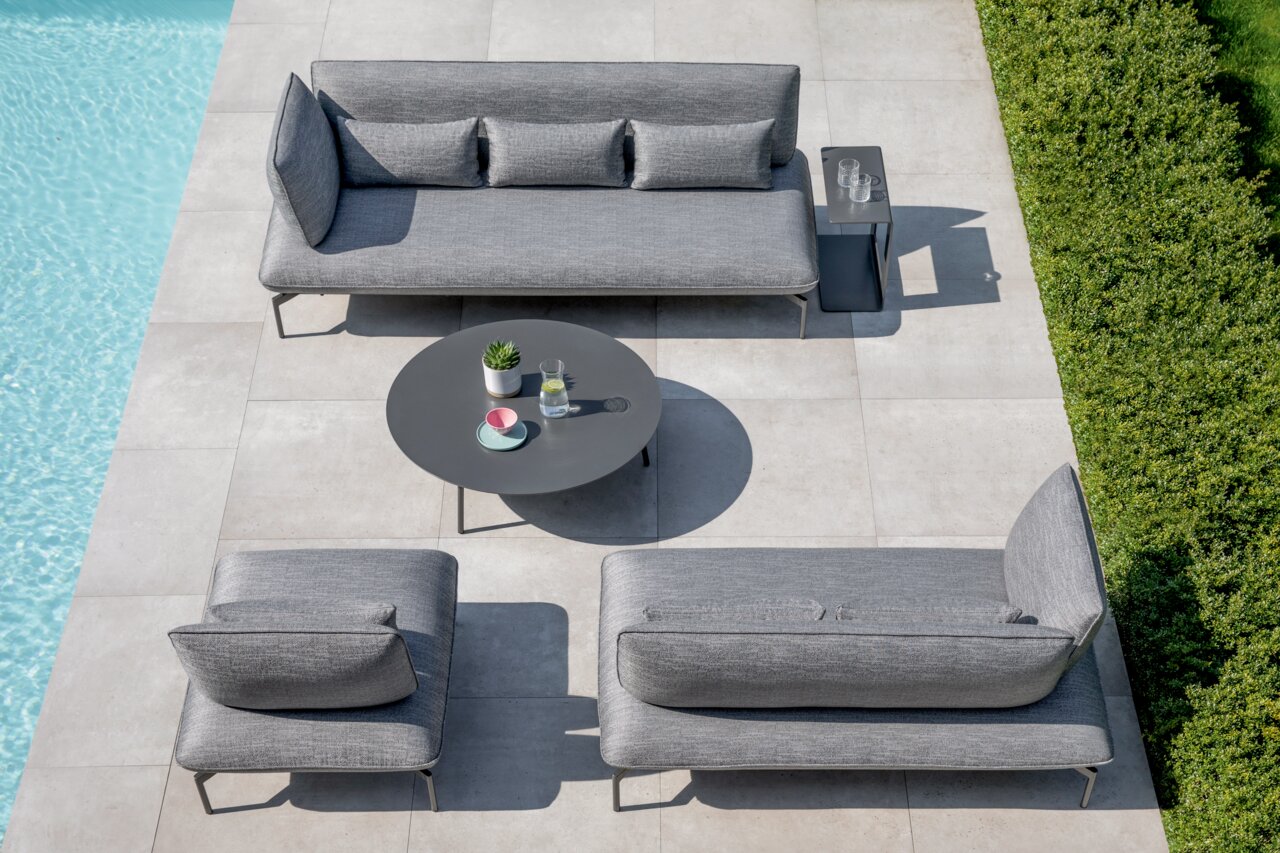 Moderne loungemeubels voor buiten in grijs, bestaande uit een loungestoel, een 2-zits- en een 3-zits loungebank en een ronde loungetafel, gefotografeerd vanuit vogelperspectief.