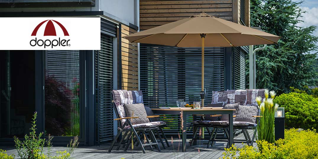 Terrassenset mit Tisch, Stühlen und einem großen Sonnenschirm, umgeben von Pflanzen und einem modernen Holzgebäude.