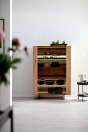 Highboard aus Holz mit Glastüren, dekoriert mit Gläsern und Schalen, in einem modernen Wohnzimmer aus der Frontalperspektive.