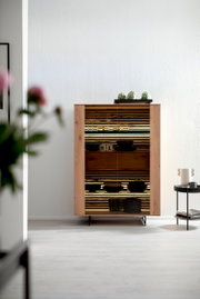 Houten hoogkast met glazen deuren, versierd met glazen en schalen, in een moderne woonkamer, gezien vanuit een vooraanzicht.