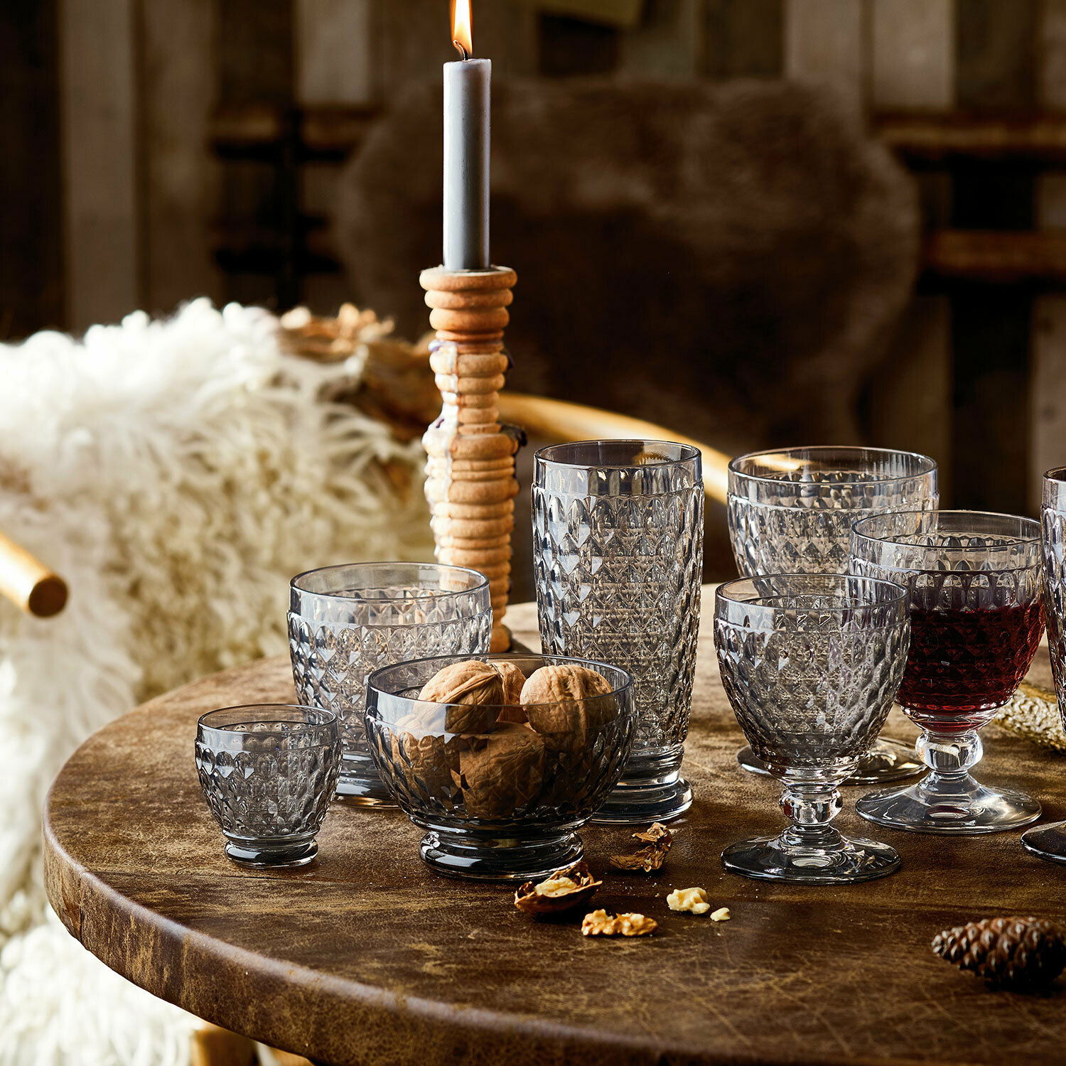 Verschiedene Boston-Gläser auf einem rustikalen Holztisch, seitliche Perspektive, mit Nüssen und einer brennenden Kerze im Hintergrund.