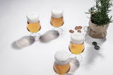 Vier Biergläser mit Schaumkrone aus der Vogelperspektive, umgeben von Brezeln und einem Kräutertopf.