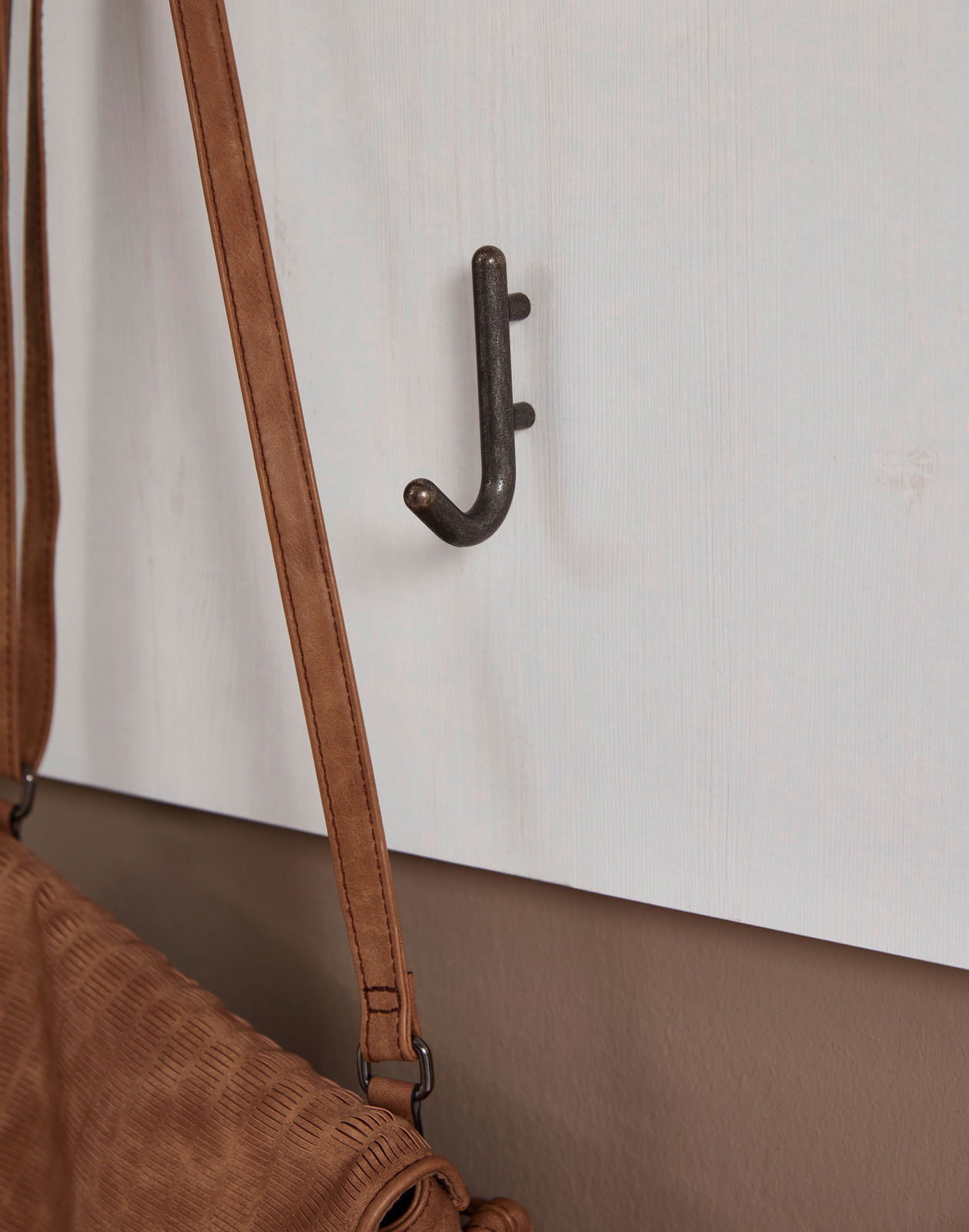 Nahaufnahme eines Garderobenhakens an einer weißen Wand mit einer braunen Tasche daran hängend, seitliche Perspektive.
