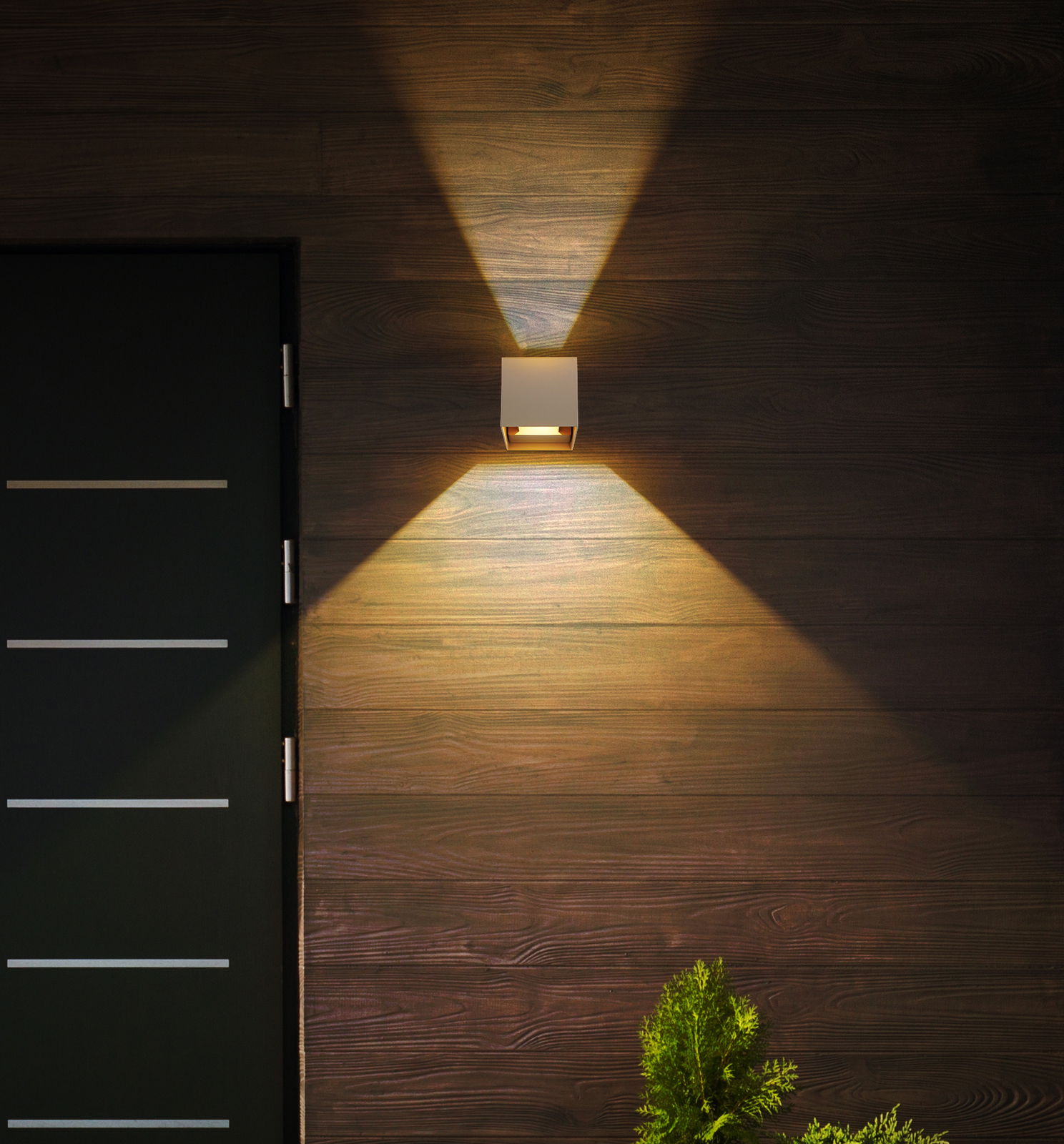 Moderne Außen-Wandleuchte an einer Holzfassade, die warmes Licht nach oben und unten abstrahlt, seitliche Perspektive.