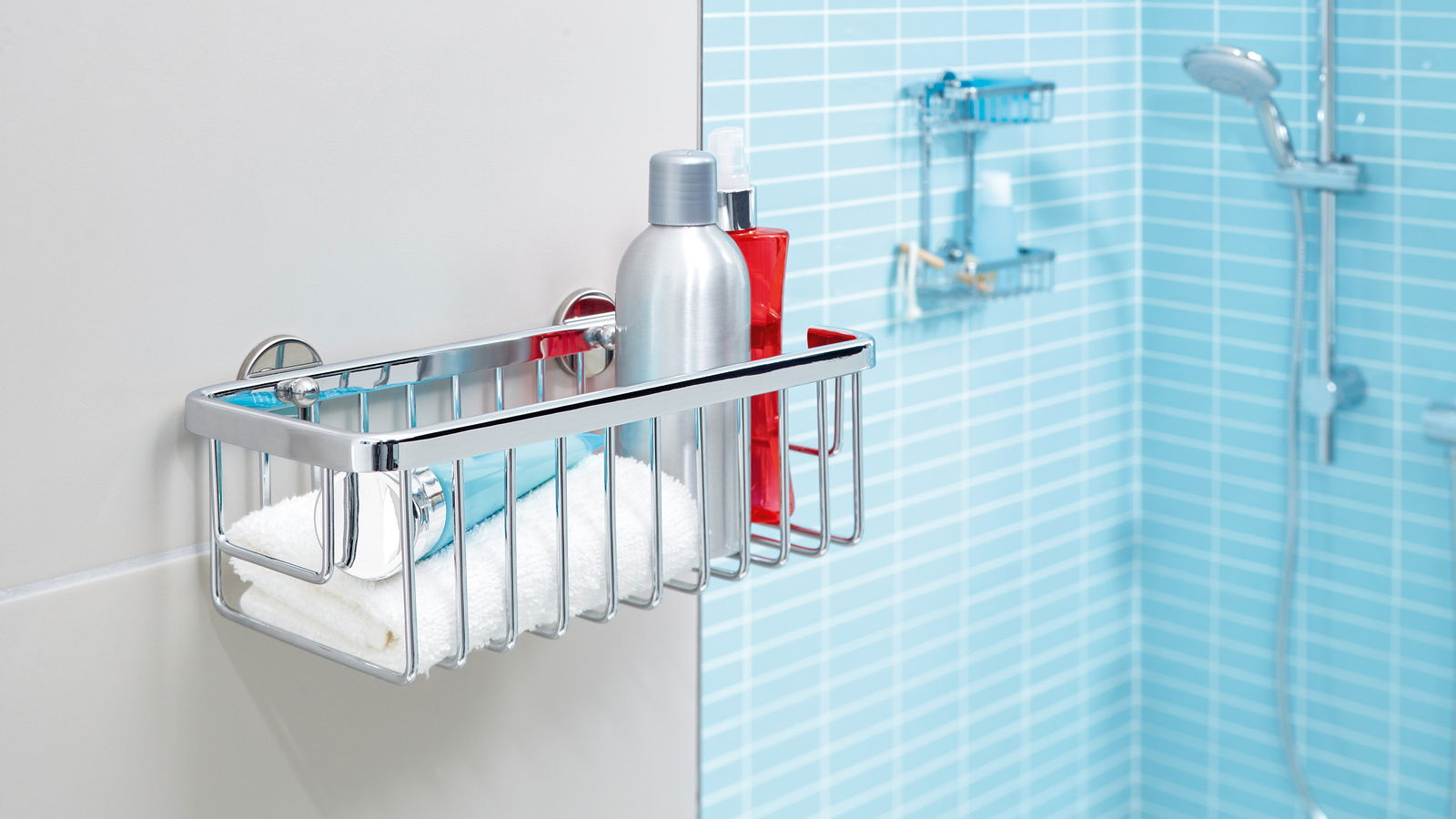 Ein einstöckiger, verchromter Duschkorb von tesa Aluxx, montiert an einer Badezimmerwand, gefüllt mit Duschutensilien. Perspektive von der Seite.