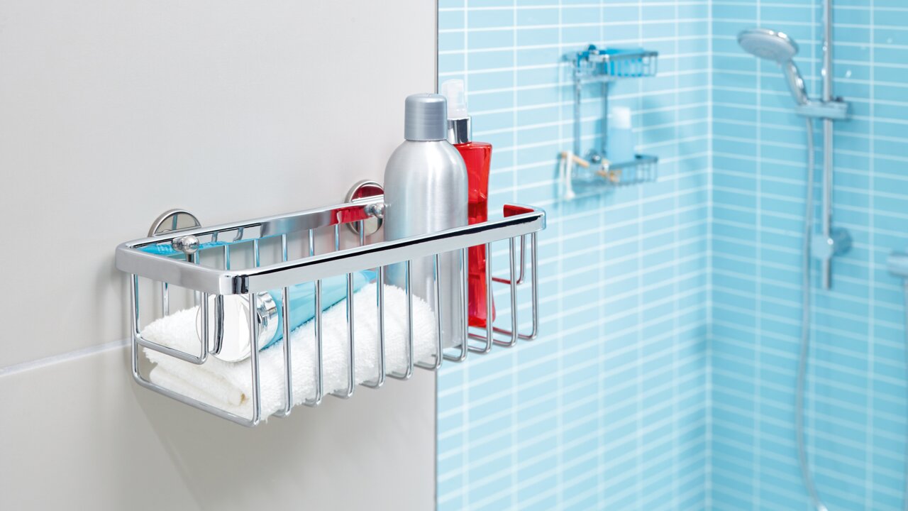Tesa Duschkorb ALUXX CHROME Ein einstöckiger, verchromter Duschkorb von tesa Aluxx, montiert an einer Badezimmerwand, gefüllt mit Duschutensilien. Perspektive von der Seite.