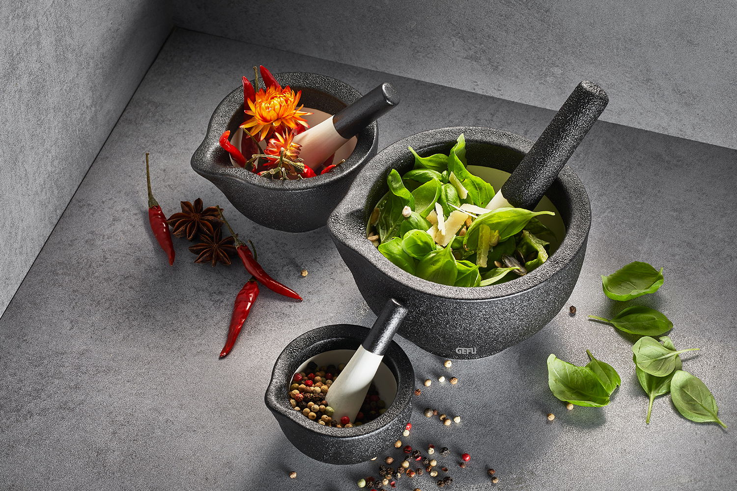 Drei Mörser in verschiedenen Größen mit Stößeln, gefüllt mit frischen Kräutern, Gewürzen und Blumen, aus der Vogelperspektive fotografiert.