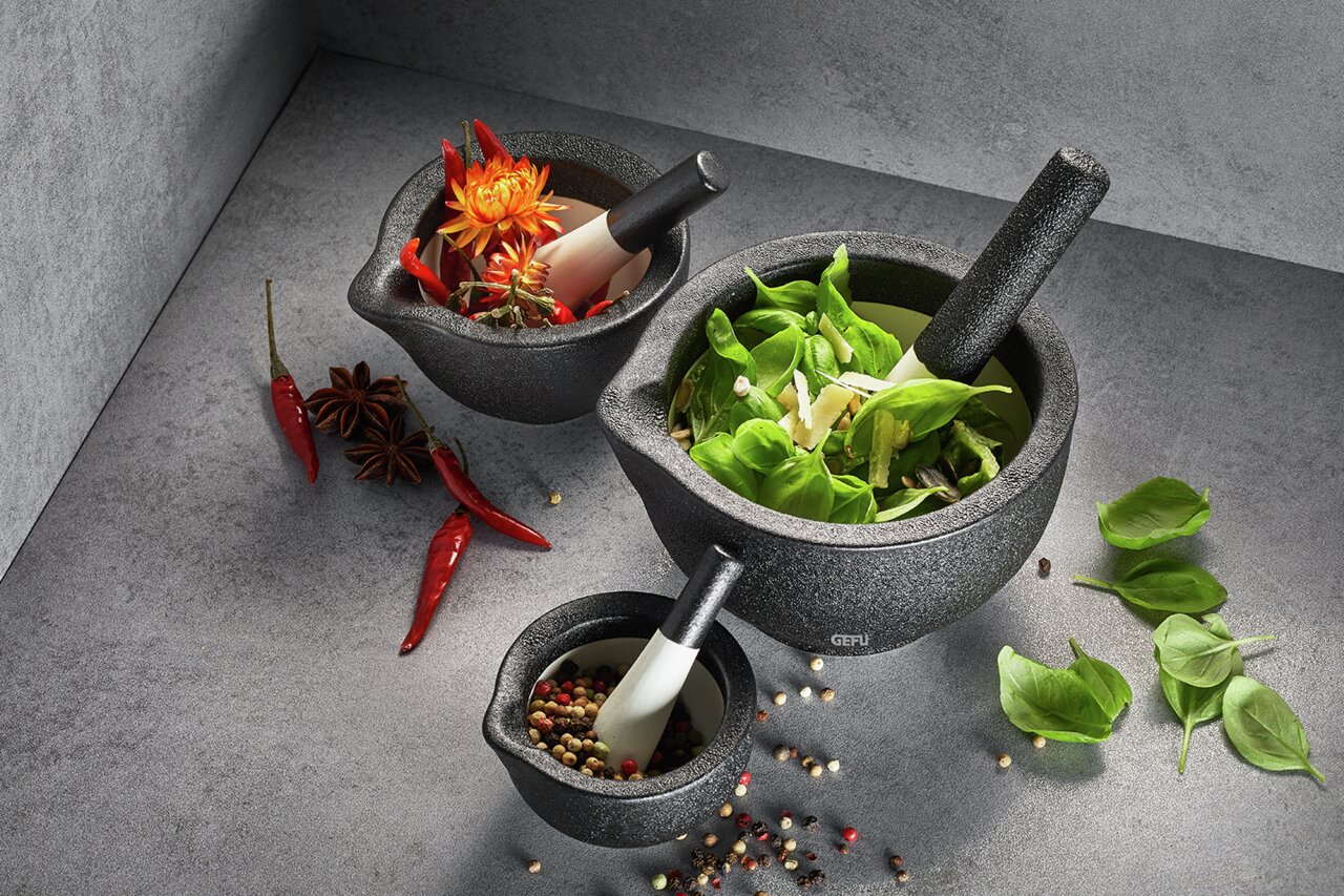 Drei Mörser in verschiedenen Größen mit Stößeln, gefüllt mit frischen Kräutern, Gewürzen und Blumen, aus der Vogelperspektive fotografiert.