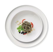 Vogelperspektive auf ein Gourmet-Set mit zwei weißen Tellern, dekoriert mit grünen Nudeln, Tomatenscheiben, Basilikumblättern und schwarzen Oliven.