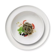 Vogelperspektive auf ein Gourmet-Set mit zwei weißen Tellern, dekoriert mit grünen Nudeln, Tomatenscheiben, Basilikumblättern und schwarzen Oliven.