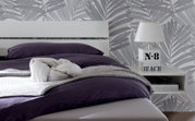 Modernes Schlafzimmer mit weißem Holz-Metall-Kopfteil, lila Bettwäsche und Nachttisch mit Lampe, seitliche Perspektive