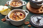 Zwei graue Mini-Cocottes mit Apfelkuchen, aus der Vogelperspektive fotografiert, umgeben von Apfelstücken und Pekannüssen.
