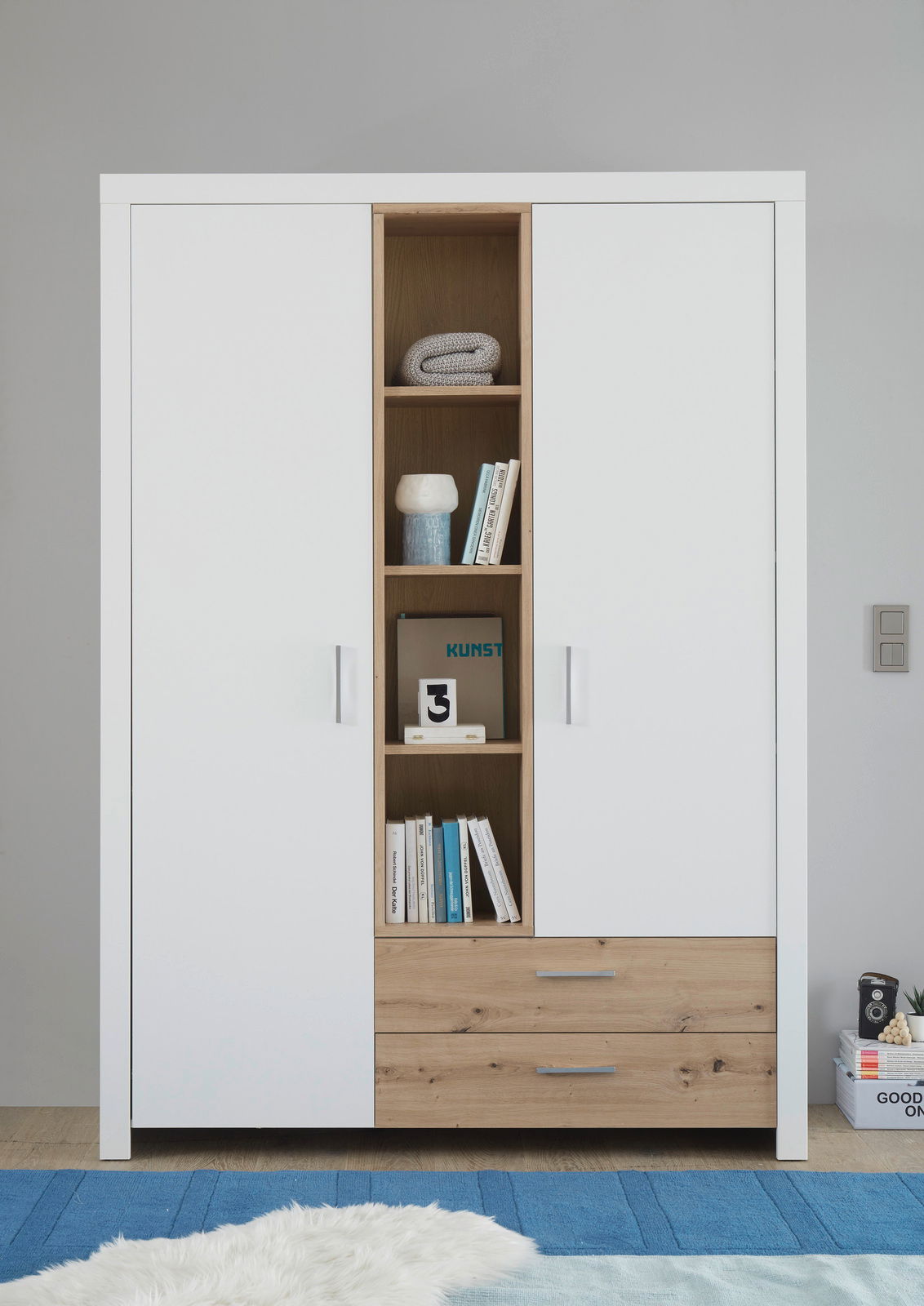 Moderner 2-türiger Drehtürenschrank in Weiß mit offenen Regalfächern in der Mitte und zwei Schubladen unten, frontal fotografiert.