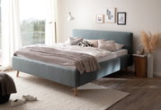 Modernes Polsterbett in einem hellen Schlafzimmer, seitliche Perspektive, mit dekorativen Kissen und einer Stehlampe.