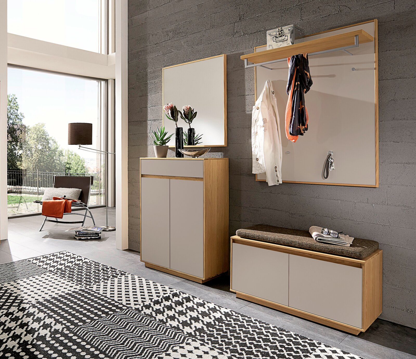 Moderne Garderobenmöbel im Flur mit Holzrahmen und hellgrauen Fronten: Schuhschrank, Sitzbank mit Polster, Wandspiegel und Garderobenpaneel mit Ablage und Kleiderhaken, fotografiert in leicht schräger Frontalperspektive.