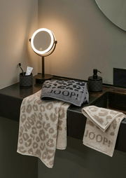 Luxuriöse Handtücher mit Leopardenmuster und JOOP!-Logo, elegant drapiert auf einem Waschtisch, beleuchtet von einem stilvollen Spiegellicht.