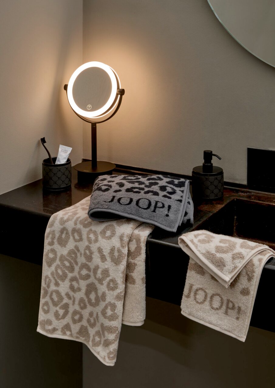 JOOP! Handtuch LEO Luxuriöse Handtücher mit Leopardenmuster und JOOP!-Logo, elegant drapiert auf einem Waschtisch, beleuchtet von einem stilvollen Spiegellicht.
