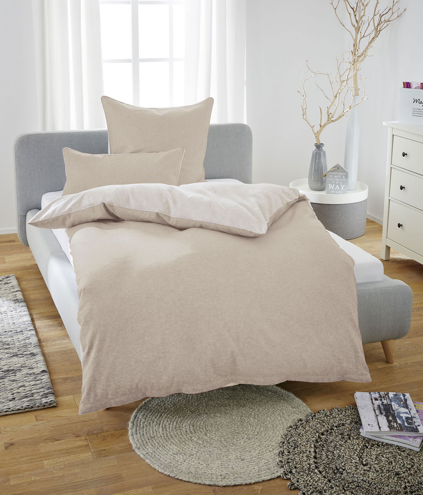 Beige Bettwäsche-Set aus Melange-Flanell auf einem grauen Bett, fotografiert aus der Vorderansicht in einem hellen Schlafzimmer.
