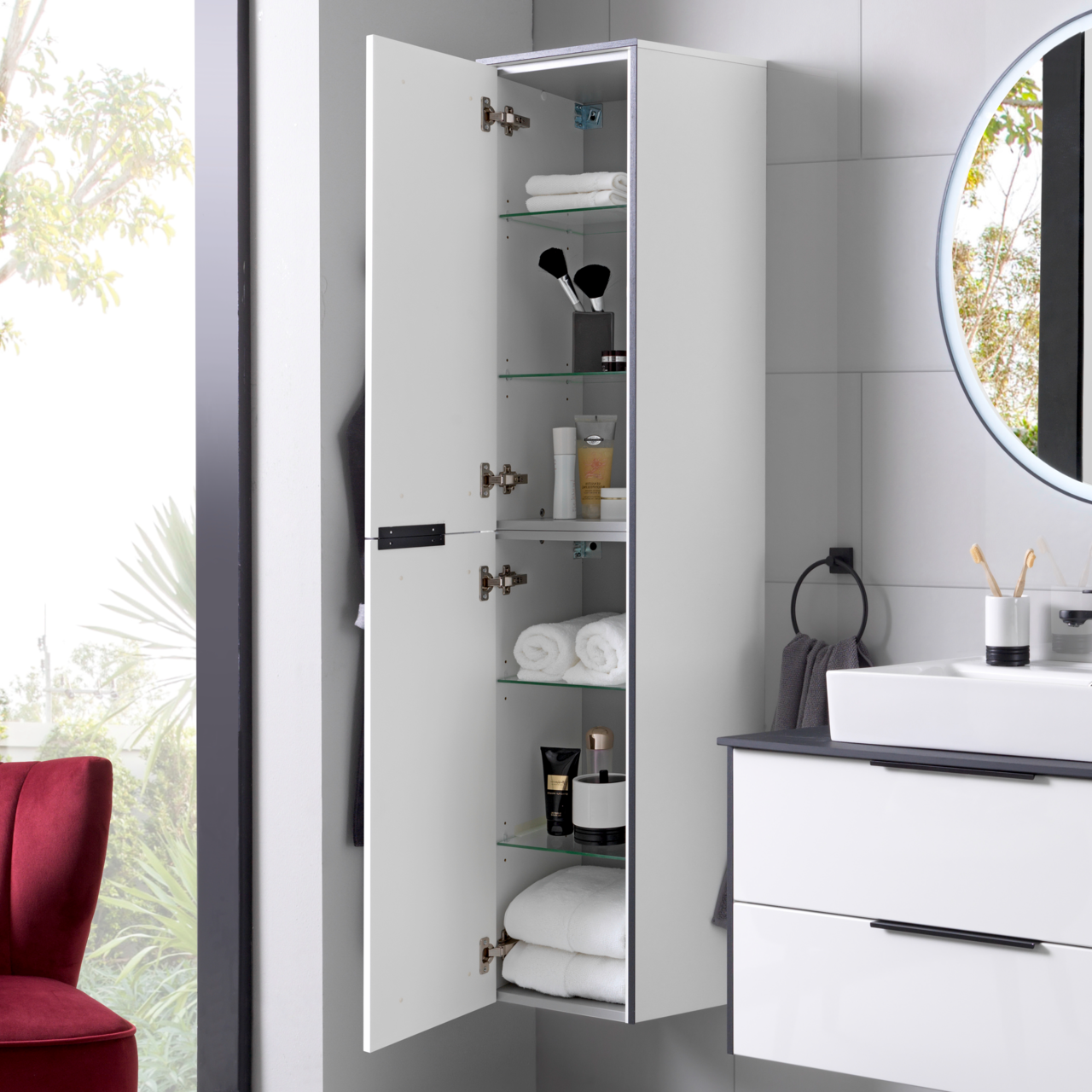 Hochschrank links mit geöffneter Tür, zeigt mehrere Glasregale mit Handtüchern und Pflegeprodukten, seitliche Perspektive