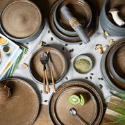 Vogelperspektive auf ein 18-teiliges Tafelservice in Beige mit rustikalem Design, bestehend aus Tellern und Schalen, dekoriert mit Besteck, Servietten und frischen Zutaten.