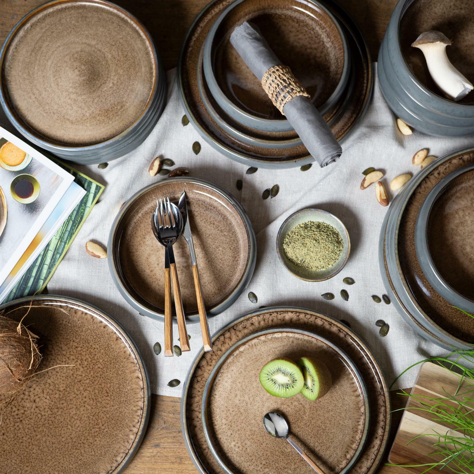 Vogelperspektive auf ein 18-teiliges Tafelservice in Beige mit rustikalem Design, bestehend aus Tellern und Schalen, dekoriert mit Besteck, Servietten und frischen Zutaten.