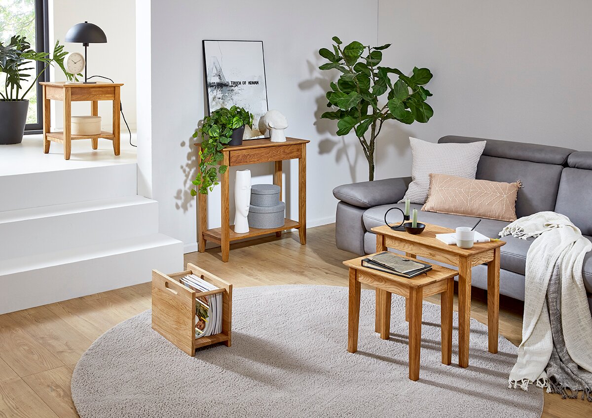 Modernes Wohnzimmer mit zwei ineinander schiebbaren Beistelltischen aus hellem Massivholz vor grauem Sofa; perspektivisch aus leicht erhöhter, schräger Vorderansicht aufgenommen.