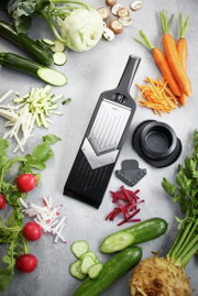 De V-schaaf Julienne VIOLI 2.0 in bovenaanzicht, omringd door gesneden groenten zoals wortelen, courgettes en radijsjes.