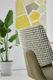 Rückansicht eines Sessels mit gemustertem Stoffbezug und grüner Lederpolsterung, im Hintergrund eine Pflanze und ein geometrisches Wandbild.