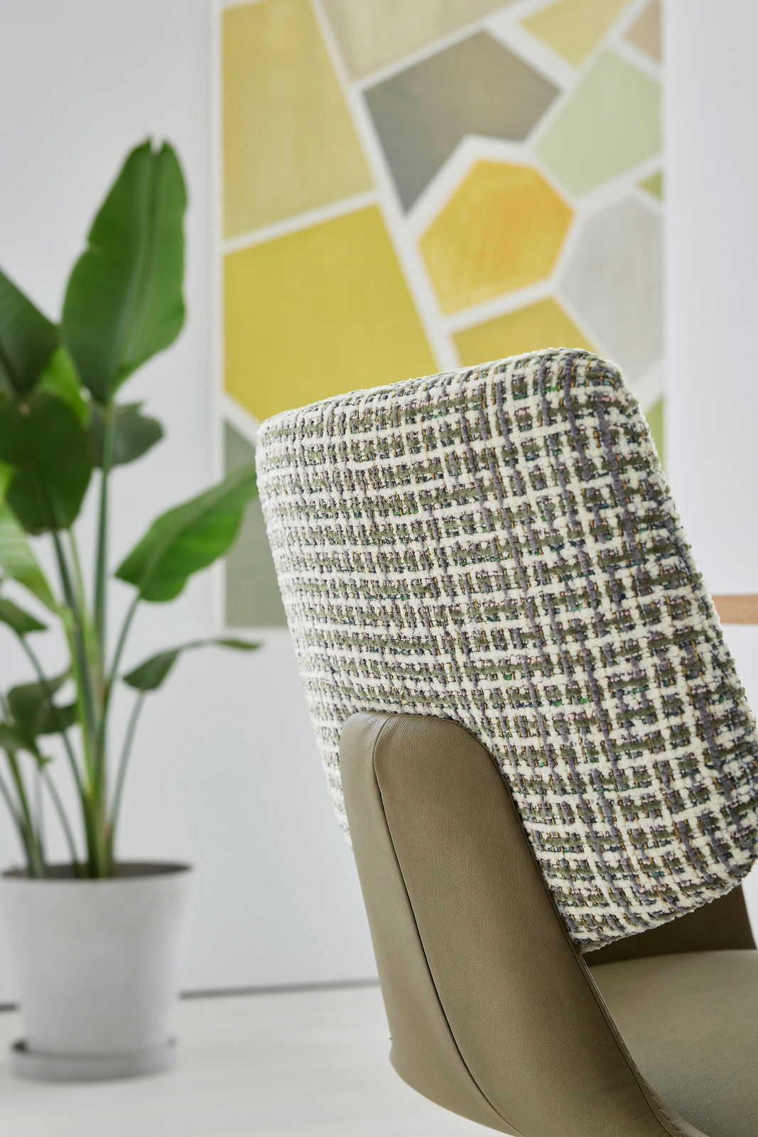 Rückansicht eines Sessels mit gemustertem Stoffbezug und grüner Lederpolsterung, im Hintergrund eine Pflanze und ein geometrisches Wandbild.