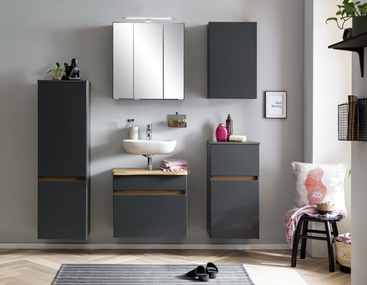 XORA Unterschrank VILLACH Moderne Badezimmermöbel in dunklem Grau mit Holzdetails, bestehend aus einem Unterschrank, einem Waschbeckenunterschrank und einem hohen Schrank, frontal betrachtet.