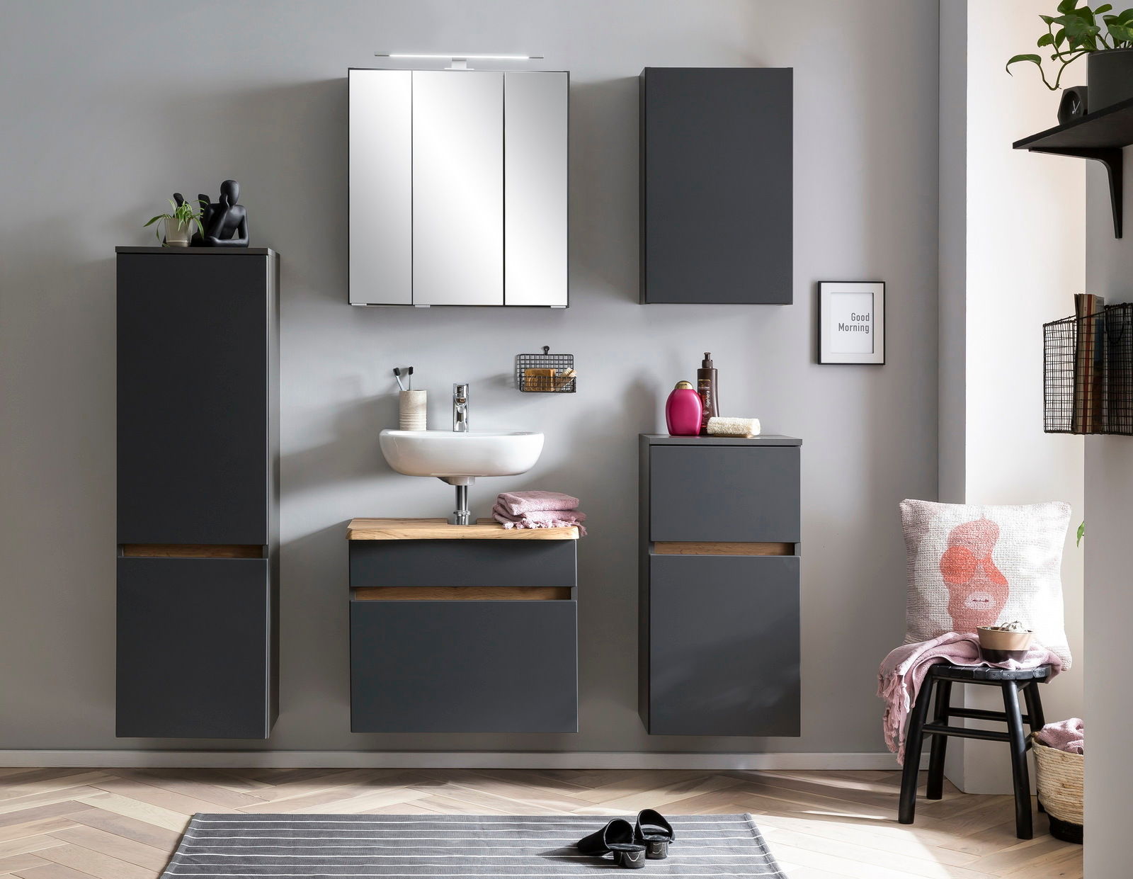 Moderne Badezimmermöbel in dunklem Grau mit Holzdetails, bestehend aus einem Unterschrank, einem Waschbeckenunterschrank und einem hohen Schrank, frontal betrachtet.