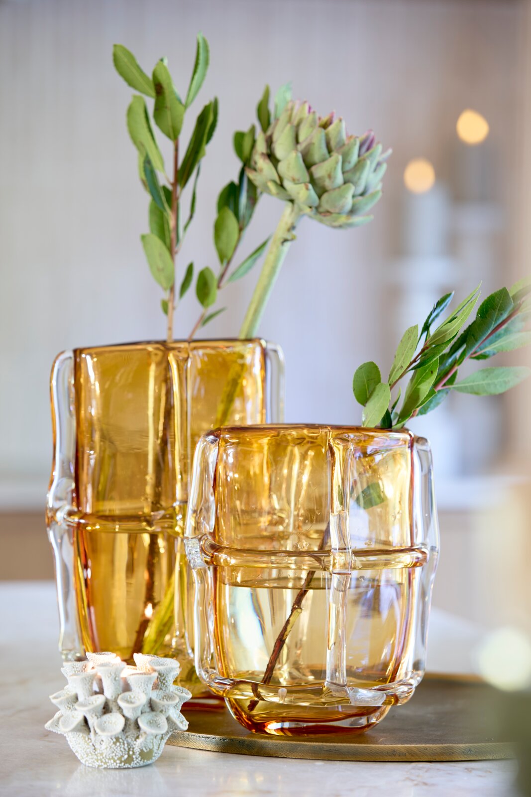 Light&Living Teelichthalter 7,50cm DELARA Zwei bernsteinfarbene Teelichthalter aus Glas in modernem Design, gefüllt mit Wasser und dekorativen Zweigen, auf einem Tisch aus der Seitenperspektive fotografiert.