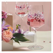 Zwei elegante Weingläser mit floralen Mustern, gefüllt mit einem rosafarbenen Getränk, umgeben von Blumen, aus einer seitlichen Perspektive fotografiert.
