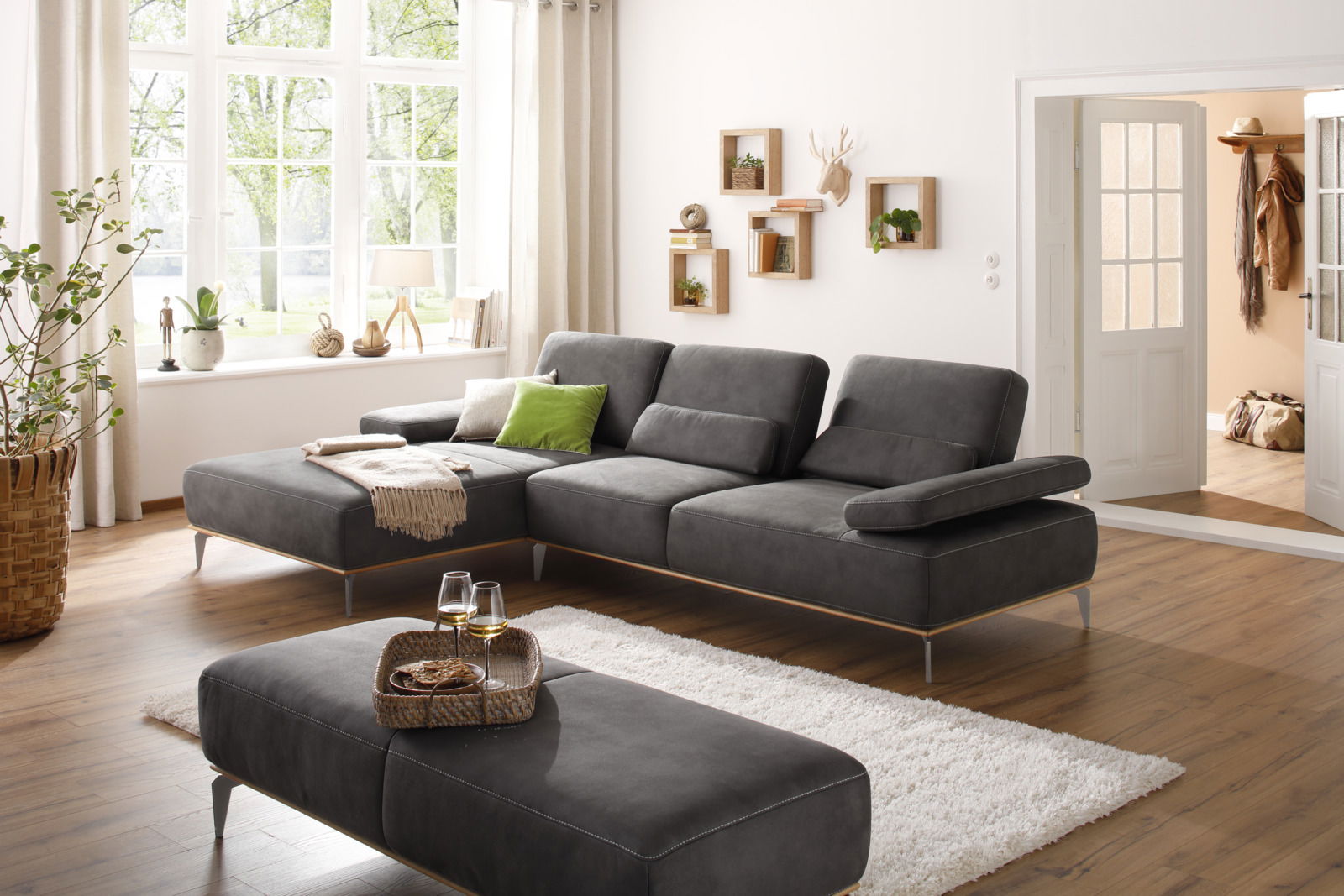 Valnatura Longchairkombination 16580 SPRINT Graue Longchairkombination in einem hellen Wohnzimmer mit großen Fenstern, Holzboden und dekorativen Elementen, seitliche Perspektive.