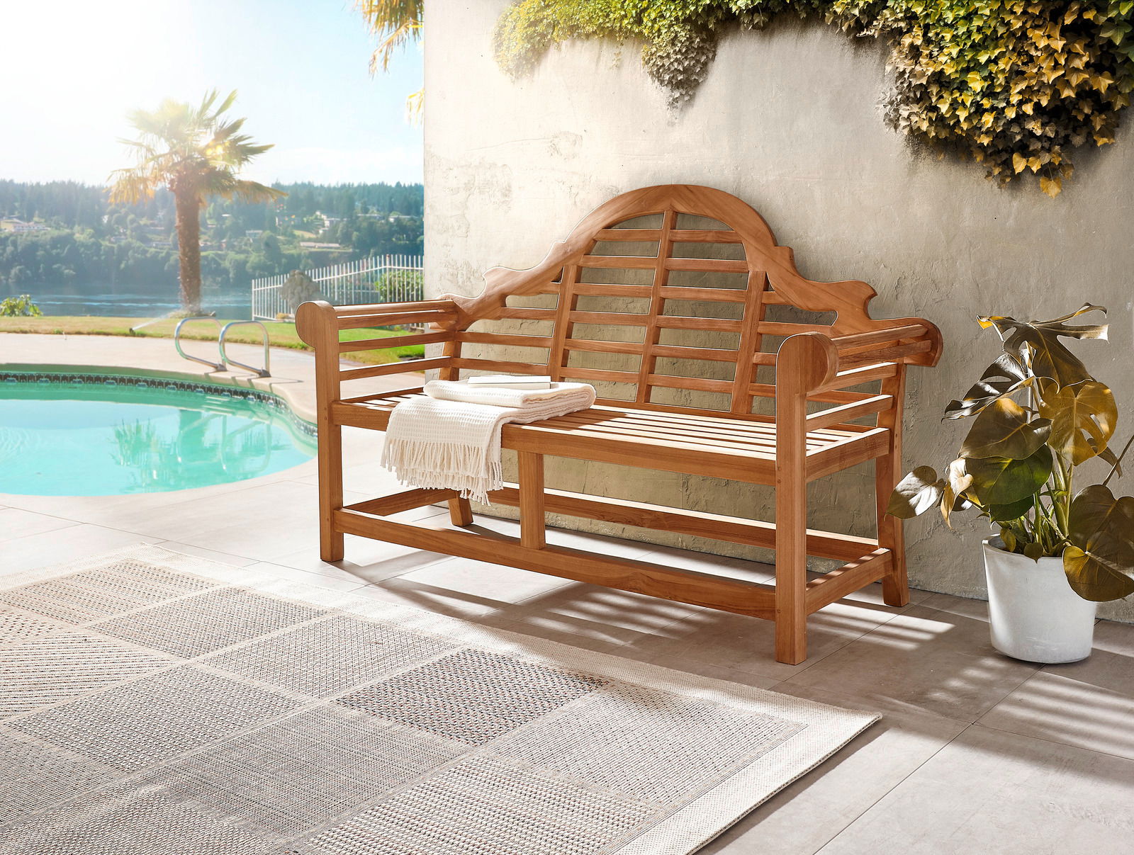 Holzbank mit geschwungener Rückenlehne und Armlehnen, auf einer Terrasse neben einem Pool, umgeben von Pflanzen, aus seitlicher Perspektive fotografiert.