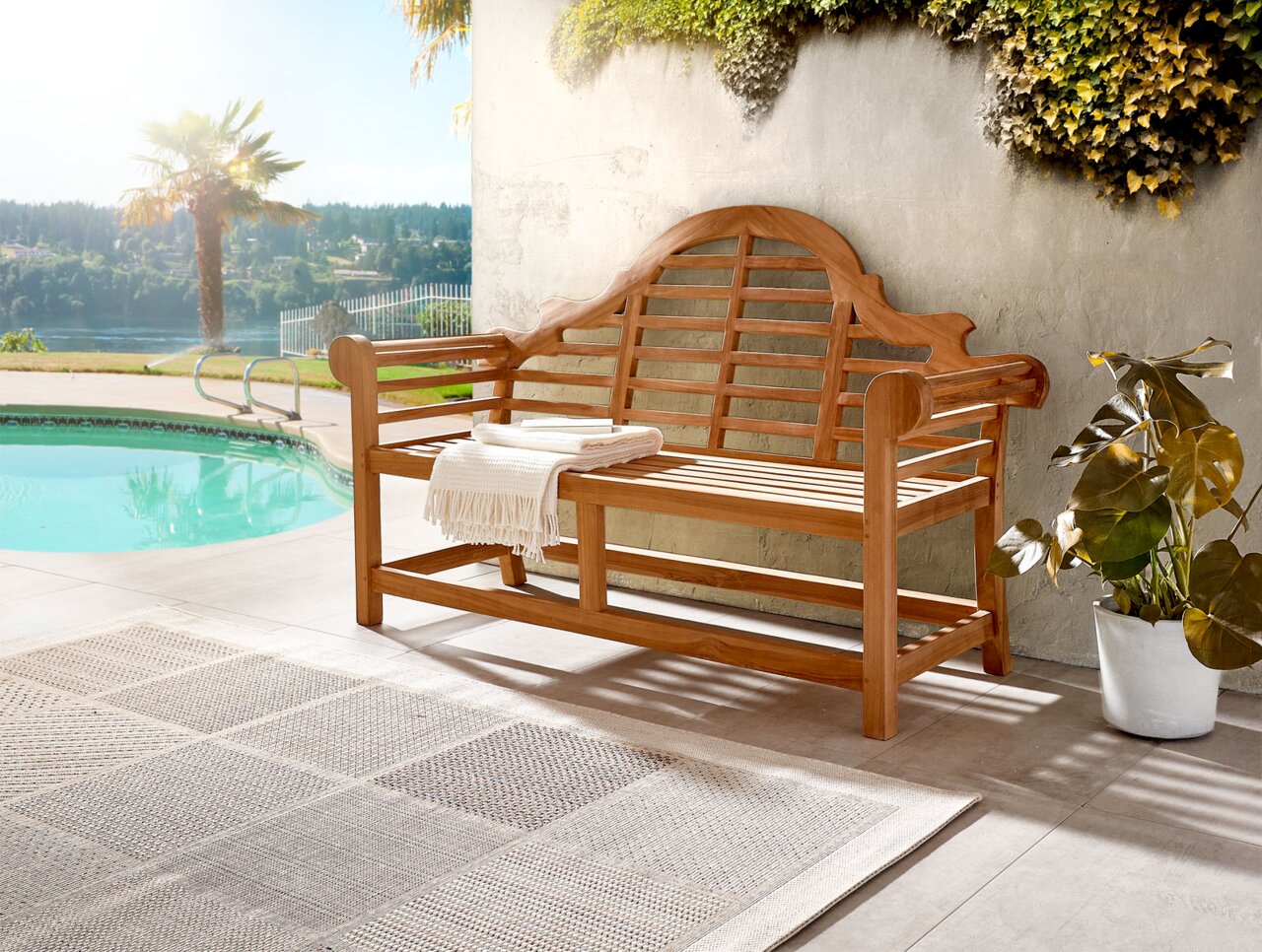 Holzbank mit geschwungener Rückenlehne und Armlehnen, auf einer Terrasse neben einem Pool, umgeben von Pflanzen, aus seitlicher Perspektive fotografiert.