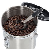 Edelstahl-Kaffeedose mit Löffel, gefüllt mit Kaffeebohnen, aus der Vogelperspektive.