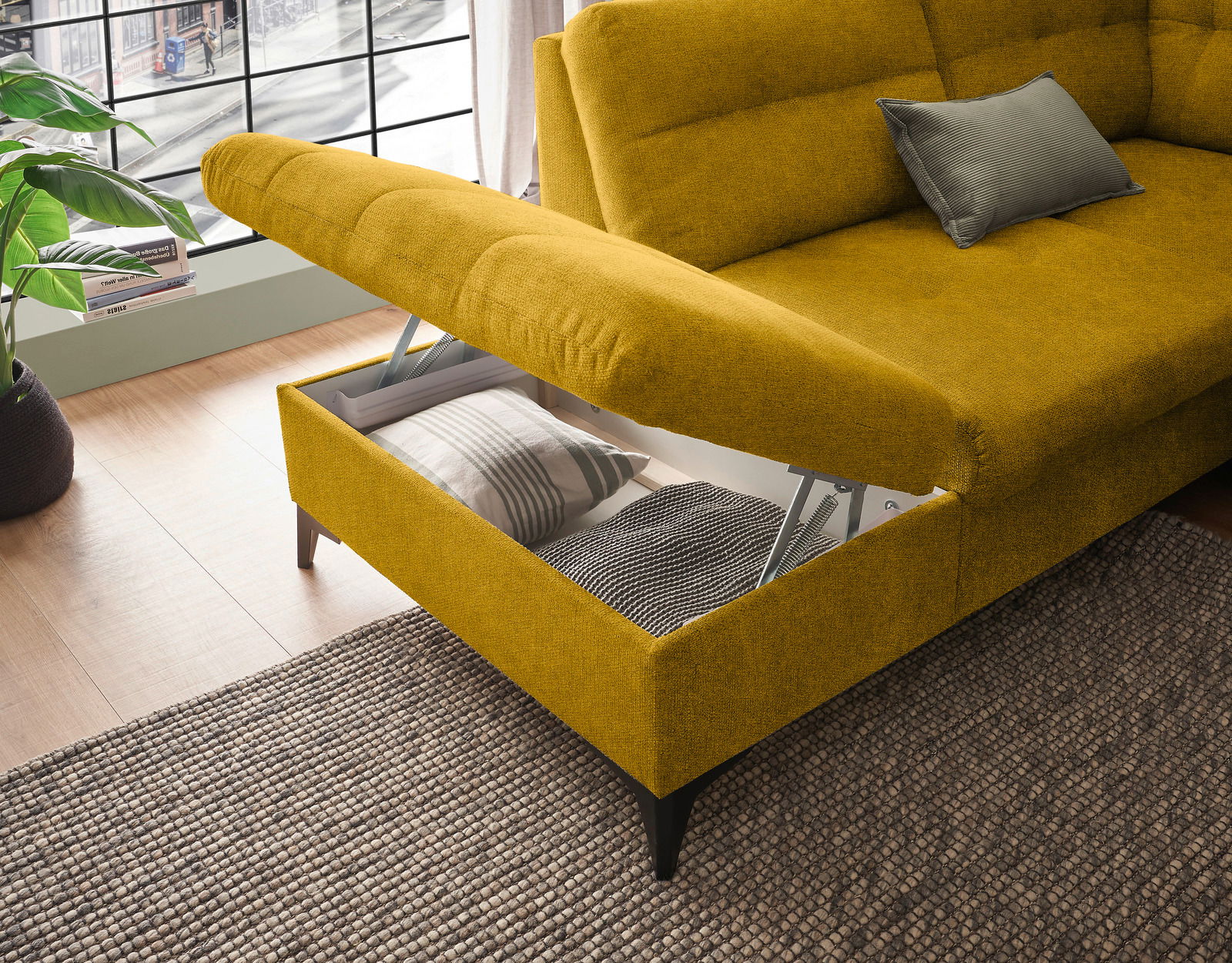 Gelbes Ecksofa mit Stauraum, geöffnet, von schräg oben fotografiert, mit Kissen und Decke im Inneren.