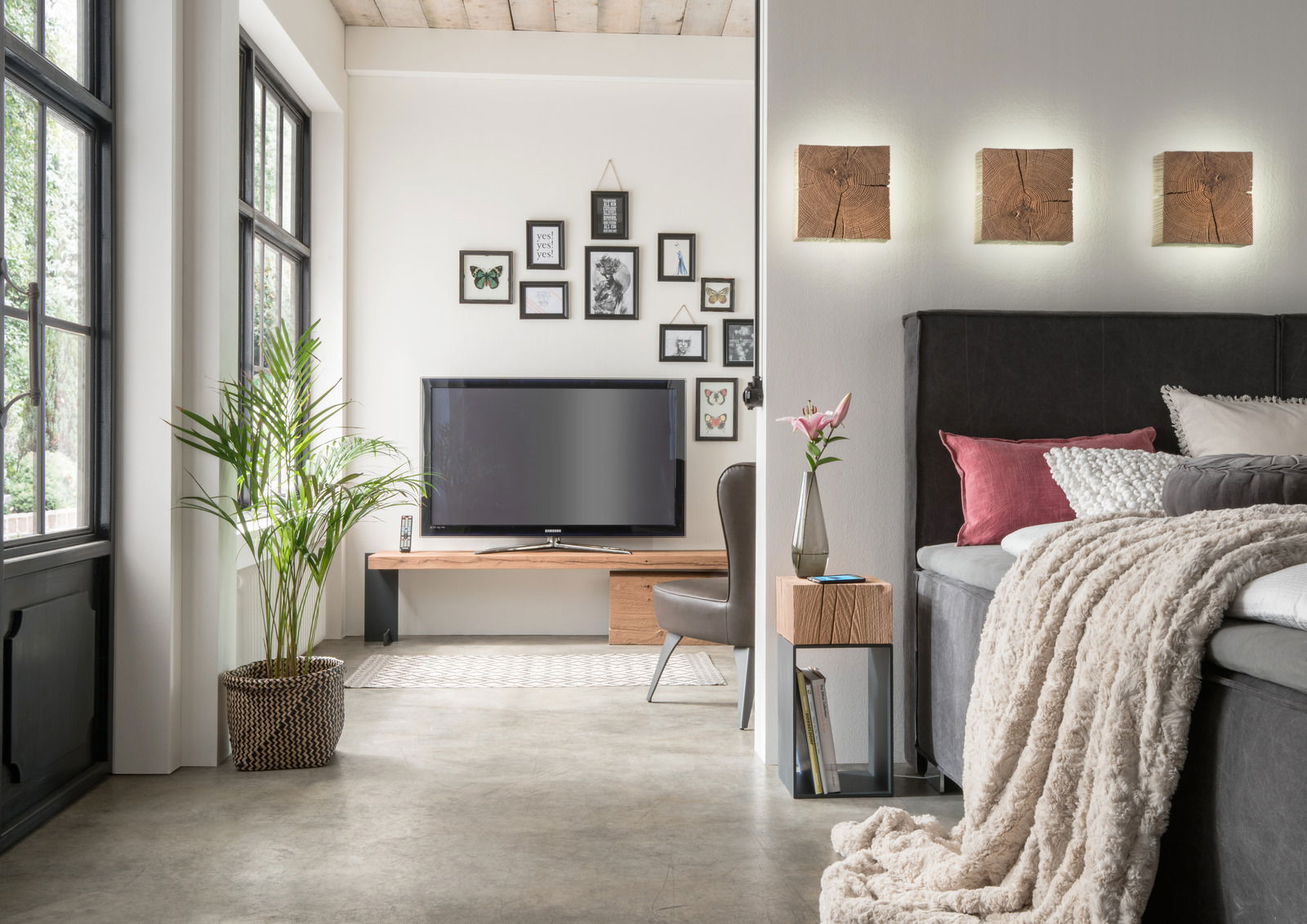 Moderne Wandleuchte aus Holz in einem stilvollen Schlafzimmer, frontal betrachtet, mit drei leuchtenden Elementen über dem Bett.