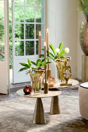 Elegante Wohnzimmerszene mit zwei goldenen Tischen, dekoriert mit modernen Vasen, Kerzen und einer Skulptur, im Vordergrund. Blick durch eine geöffnete Terrassentür auf einen grünen Garten.